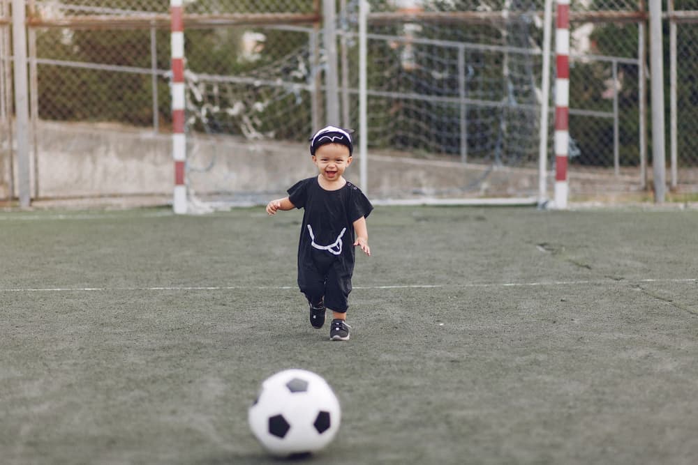 Bambino che corre ridendo verso il pallone su campo in sintetico