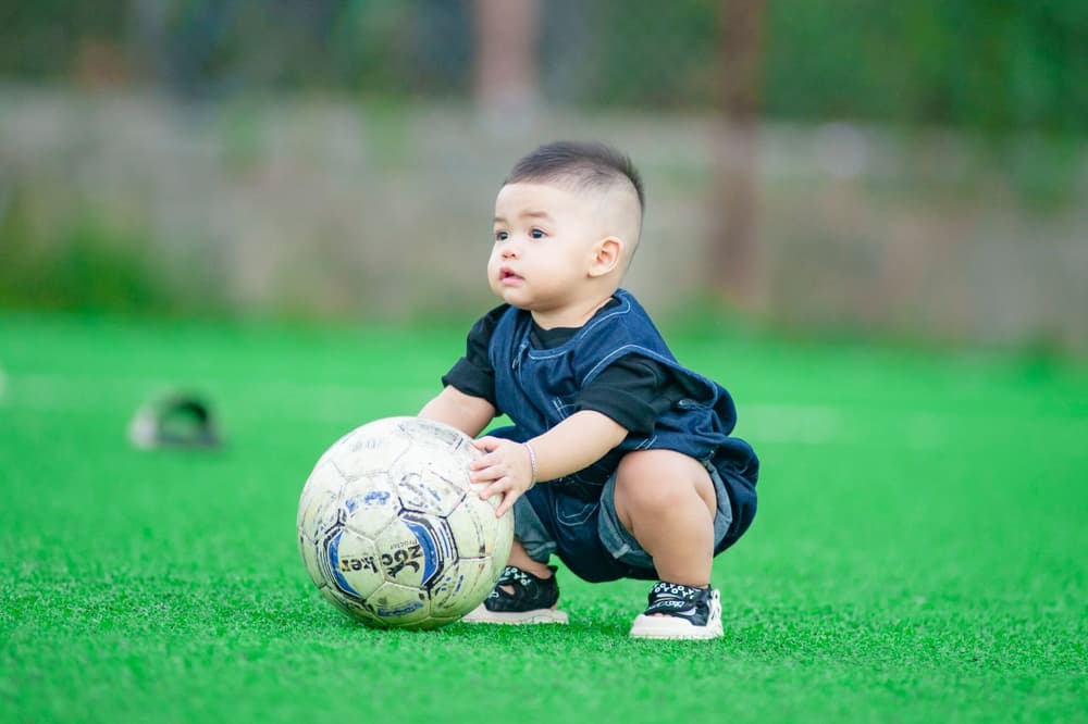 Bambino piccolo accovacciato che tiene il pallone da calcio